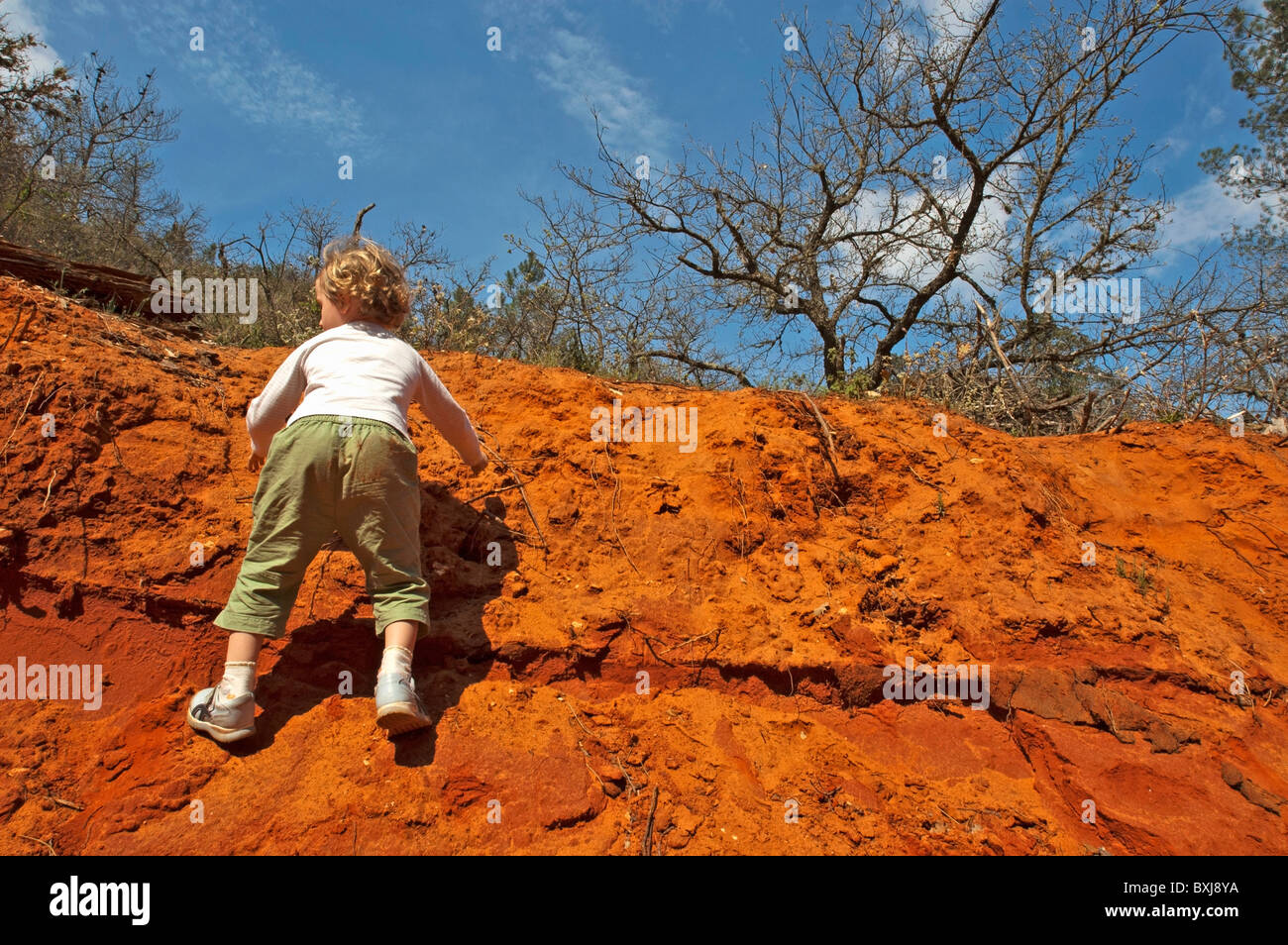 Little girl climbing up a red, sandy cliff, Rustrel, Provence, France. Stock Photo