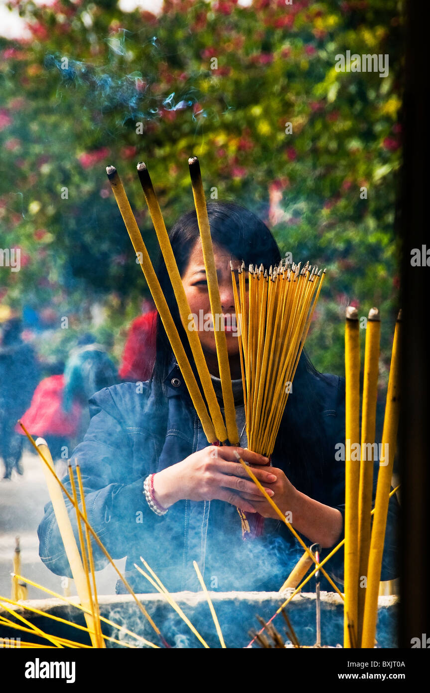 Expressive young Asian woman offering incense at Buddhist temple in Hong Kong China Stock Photo