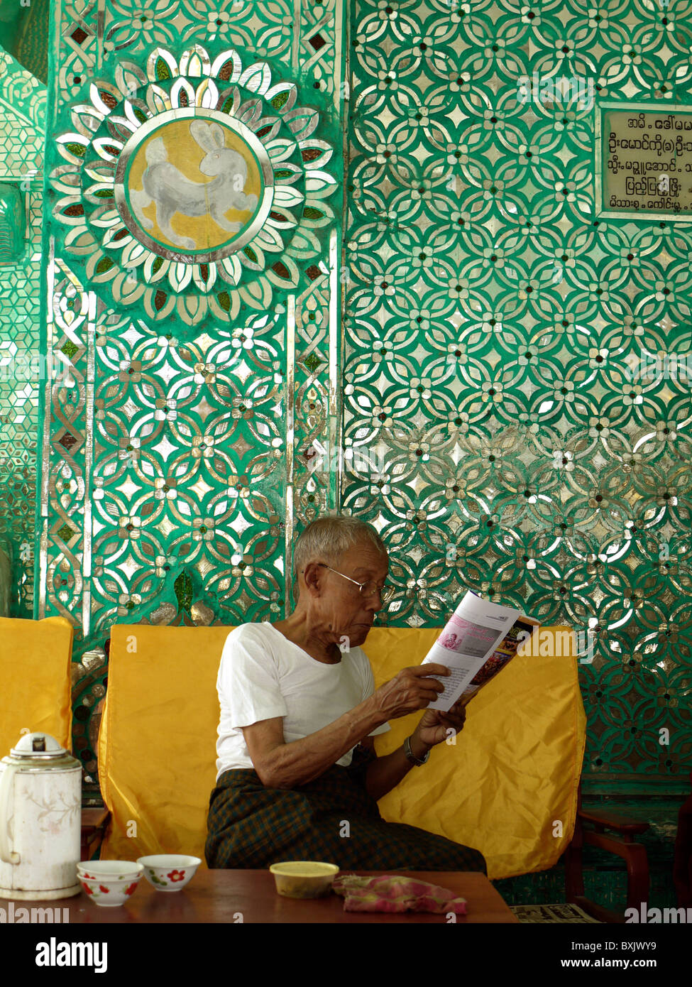 Man reading a paper in a glass decorated room in the Mandalay Palace Compound, Mandalay, Burma, Myanmar Stock Photo