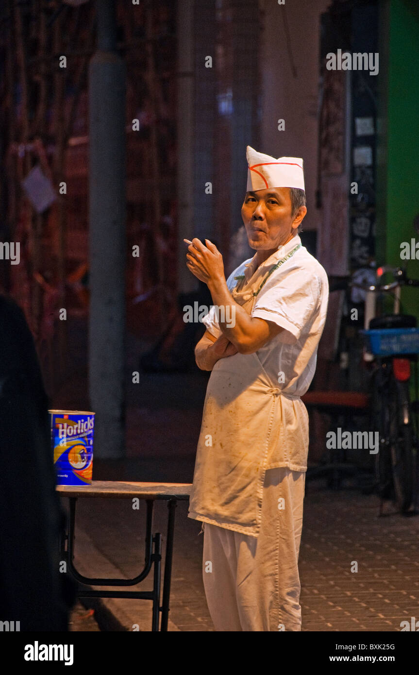 Asian male kitchen worker standing outside of restaurant smoking a cigarette in downtown Hong Kong China Stock Photo
