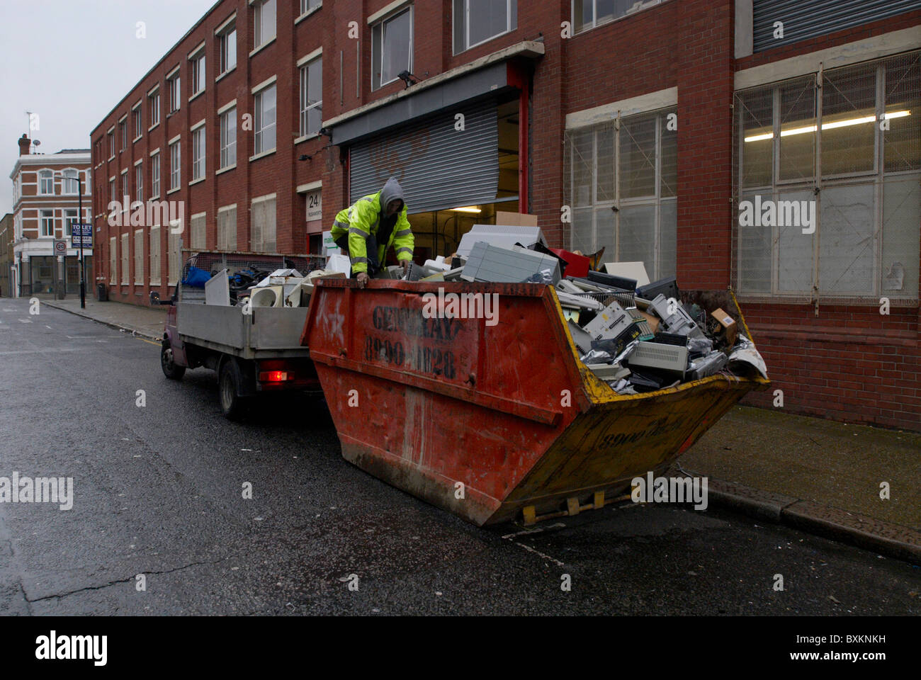 Scrap metal collectors searching through old office equipment in a skip