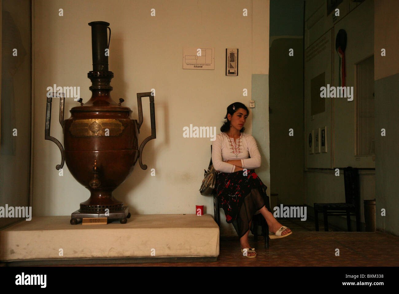 Custodian sits beside a huge Tula samovar in the museum of the Ark Fortress in Bukhara, Uzbekistan. Stock Photo