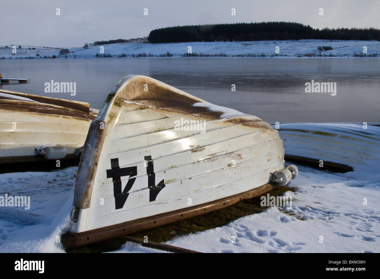 Cold winter weather snow landscape of beached upturned Stocks fishing boats,  United Utilities river reservoir lake. Trough of Bowland, Lancashire, UK Stock Photo