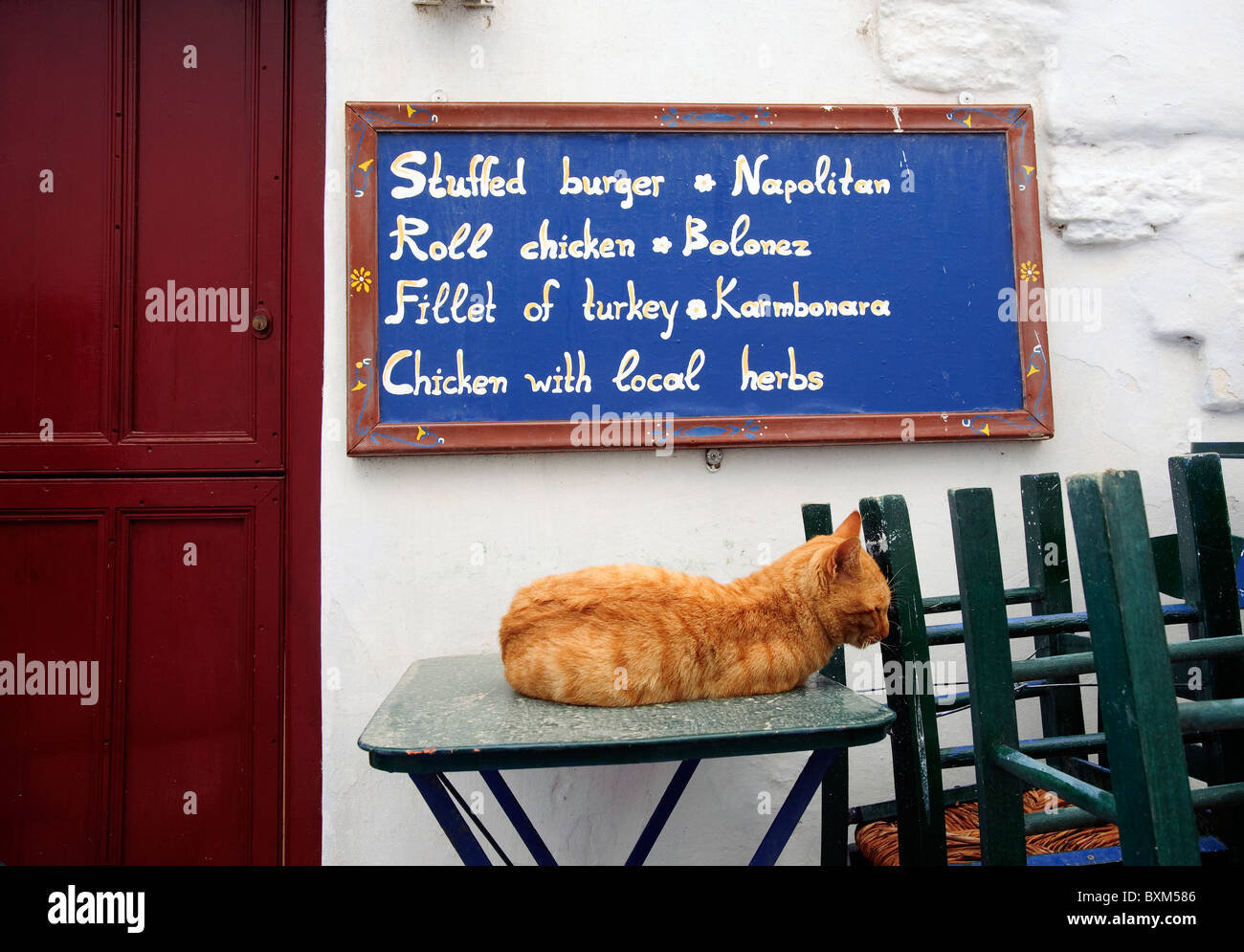 Ginger cat sleeping on one of  the tables of a small taverna's outdoors terrace in the village of Chora, Amorgos island, Greece. Stock Photo