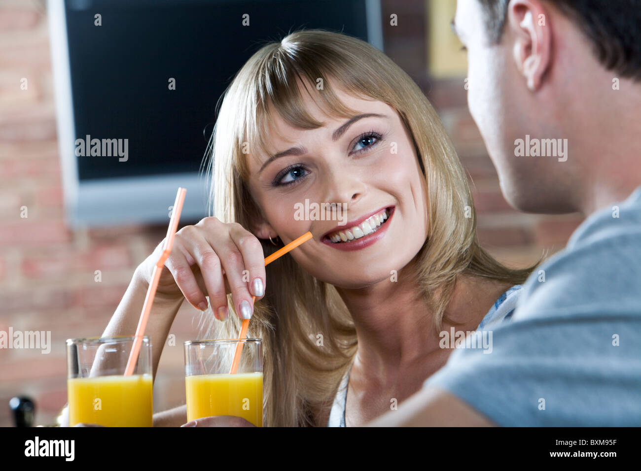 Smiling cute blond woman listening to her male companion while drinking orange juice in the bar Stock Photo