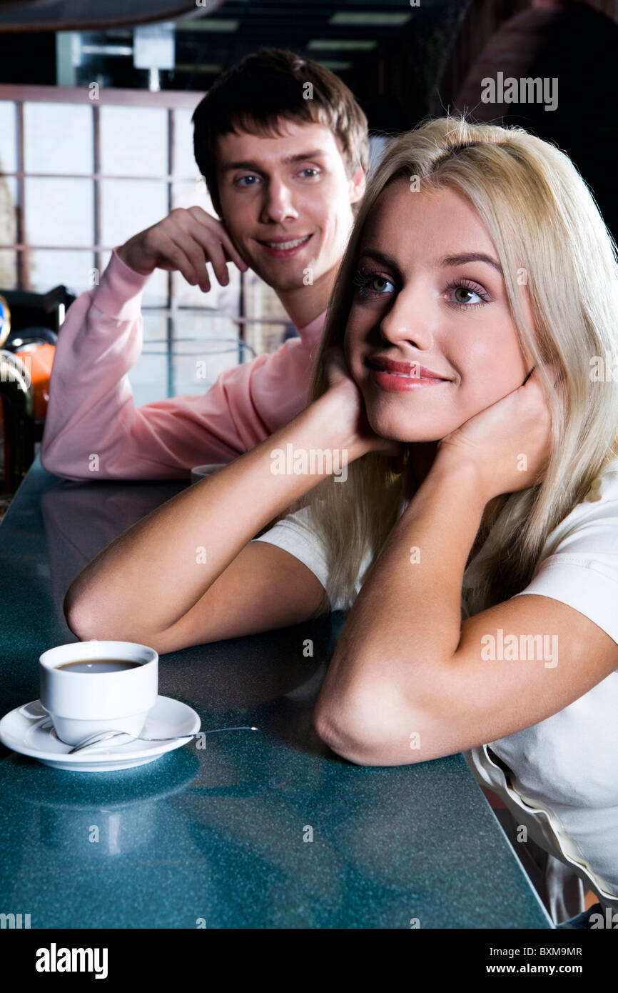 Smiling cute blond woman drinking coffee in the bar and handsome brunette man behind admiring her Stock Photo