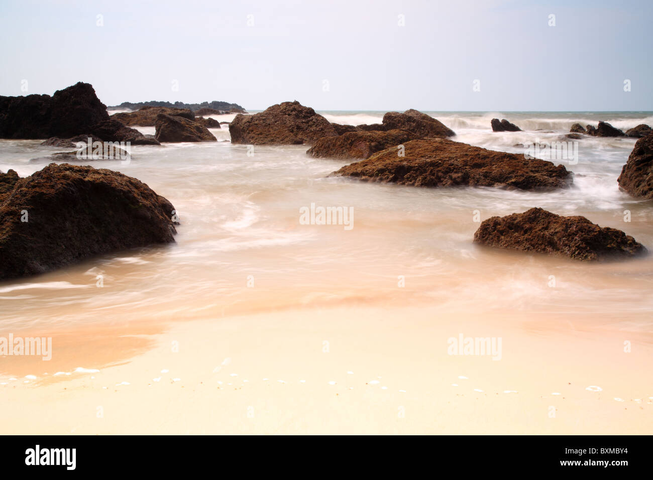Slow shutter sea around rocks on the beach Goa India Stock Photo