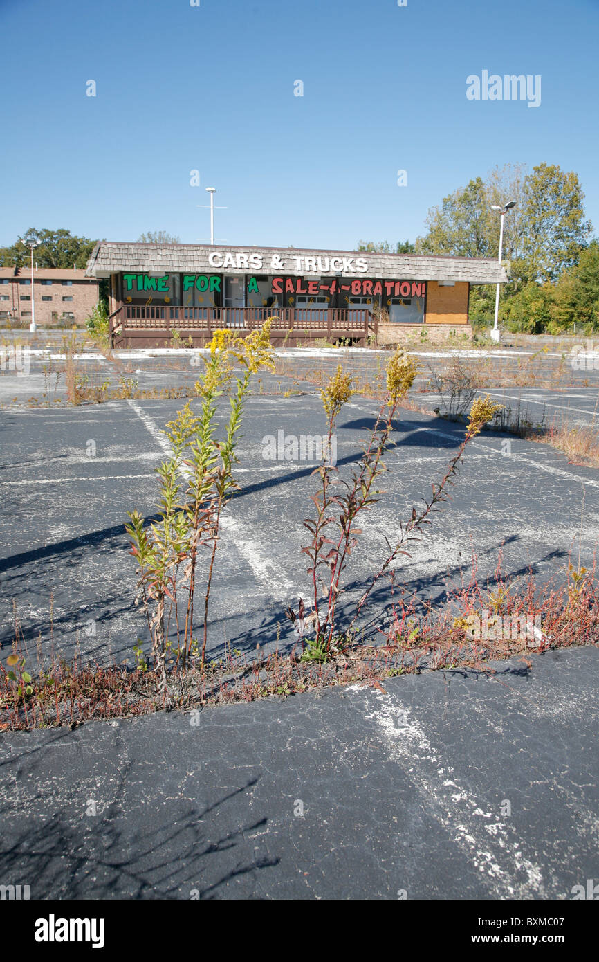 Empty abandoned car and truck dealer lot with weeds growing. Sign reads time for a sale a bration. Stock Photo