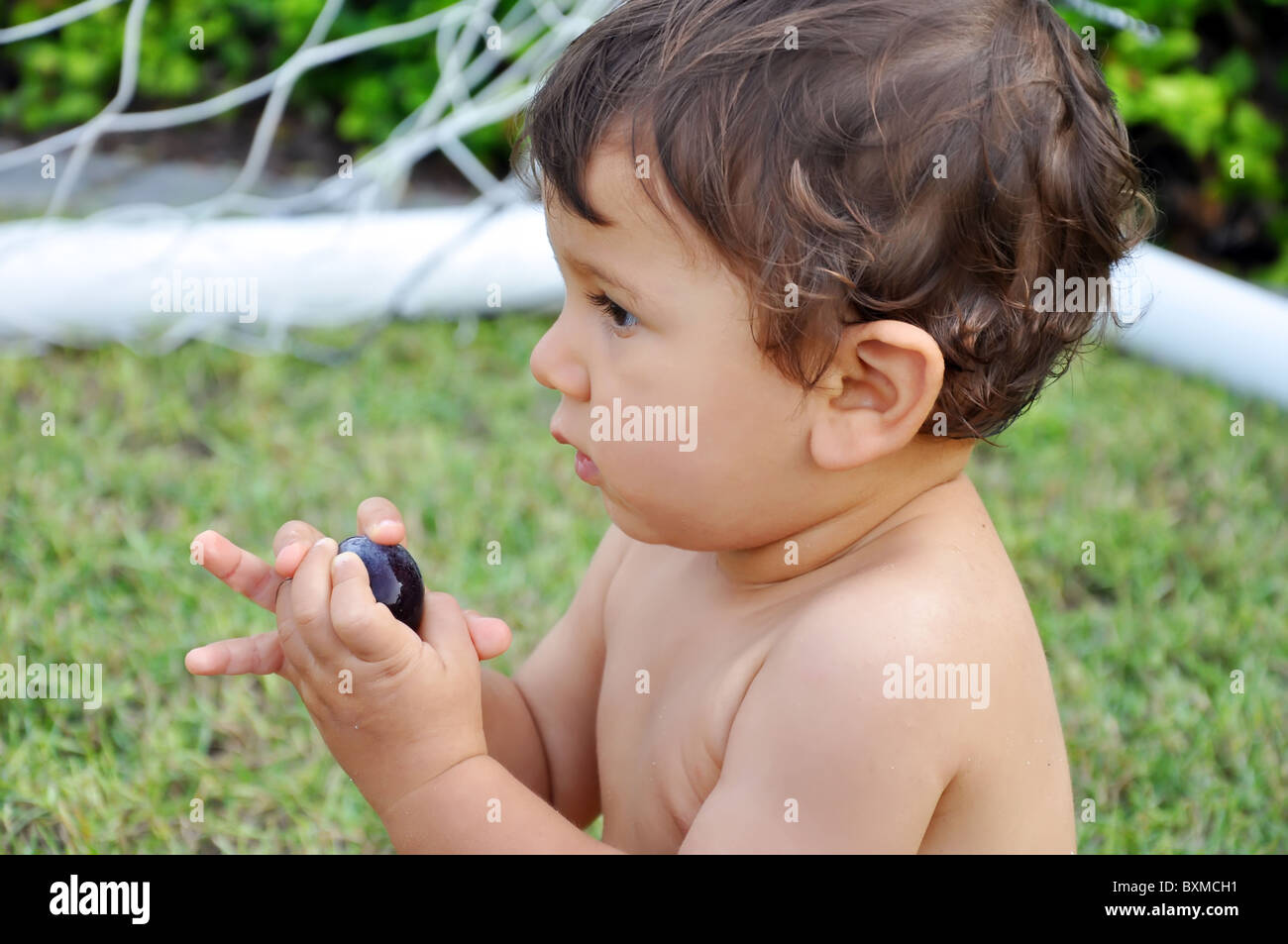 One year old boy eating grape on grass Stock Photo