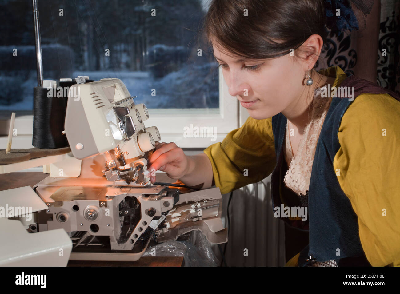 A young seamstress clean overlockery in front of window at wintertime. Stock Photo