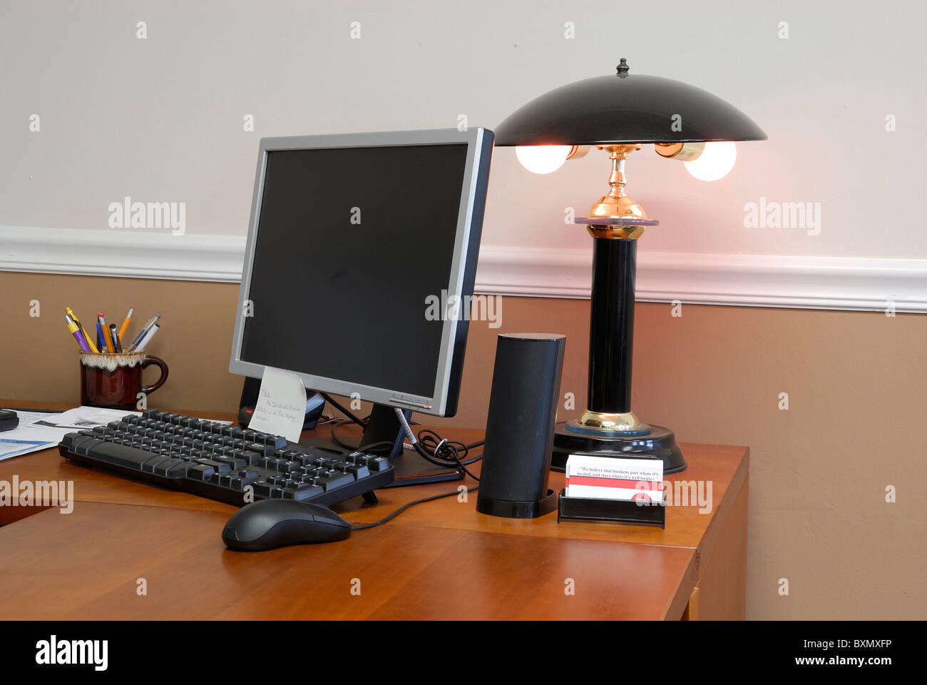 Modern office with a wooden desktop with computer keyboard and monitor and mouse. Also displaying a lamp and some paper work. Stock Photo