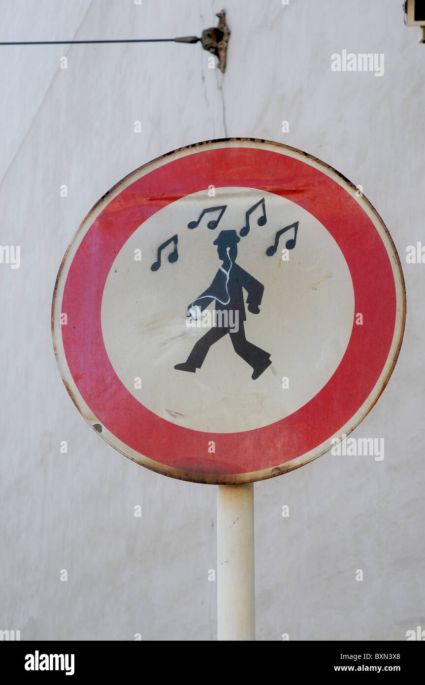 A traffic sign indicating people walking has been tampered with graffiti stenciling to show a man listening to music. Stock Photo