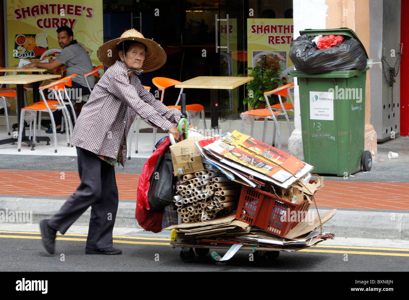 Singapore: poor woman collecting paper and kartons, pushing cart down  street Stock Photo - Alamy