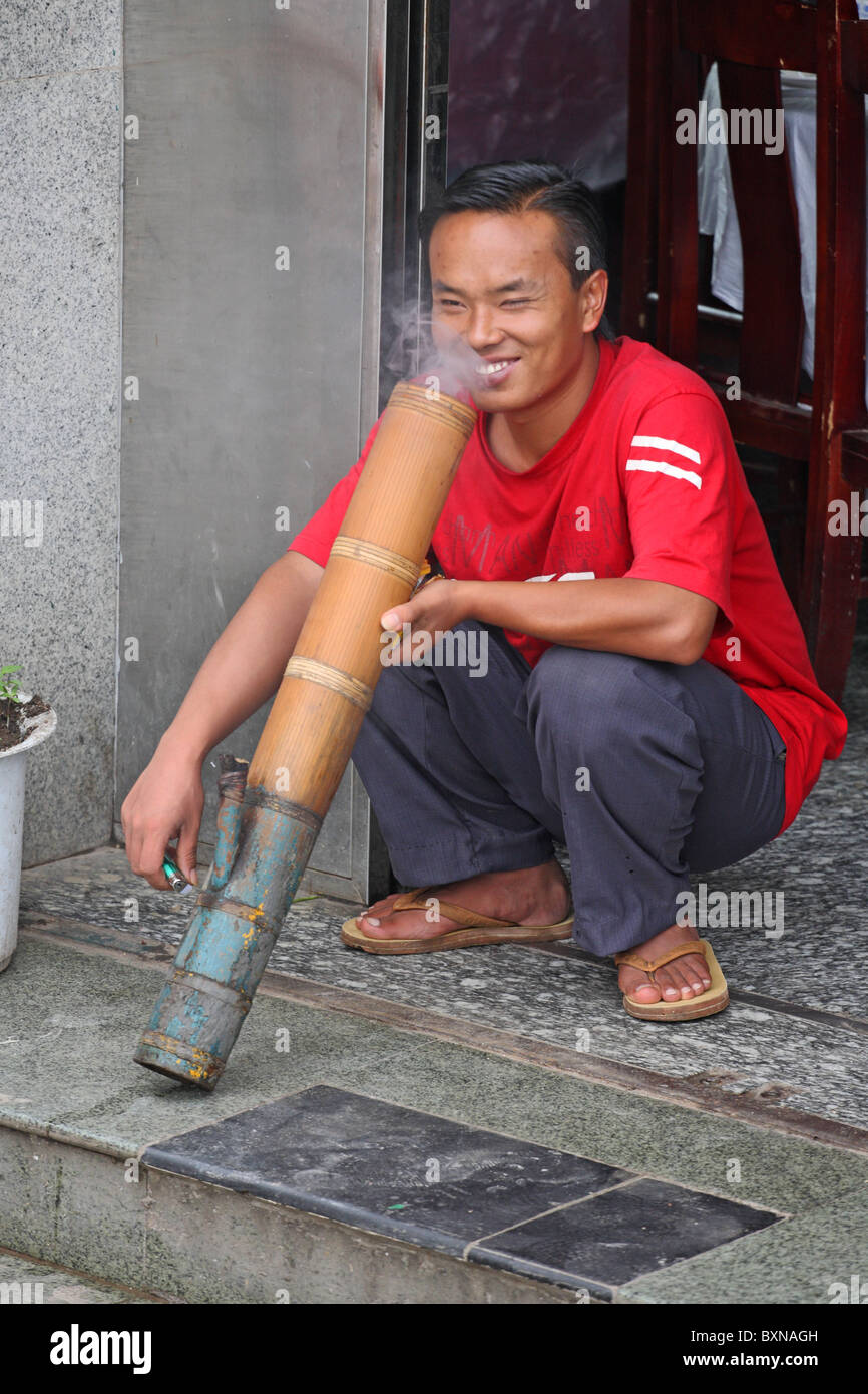 Man smoking huge bong in street, Yuanyang, Yunnan Province, China Stock Photo