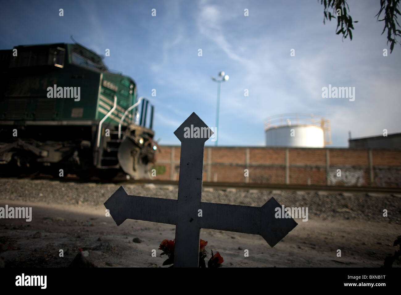 A cargo train moves across the tracks in front of a cross remembering a deceased Central American Migrant in Mexico City, Mexico Stock Photo