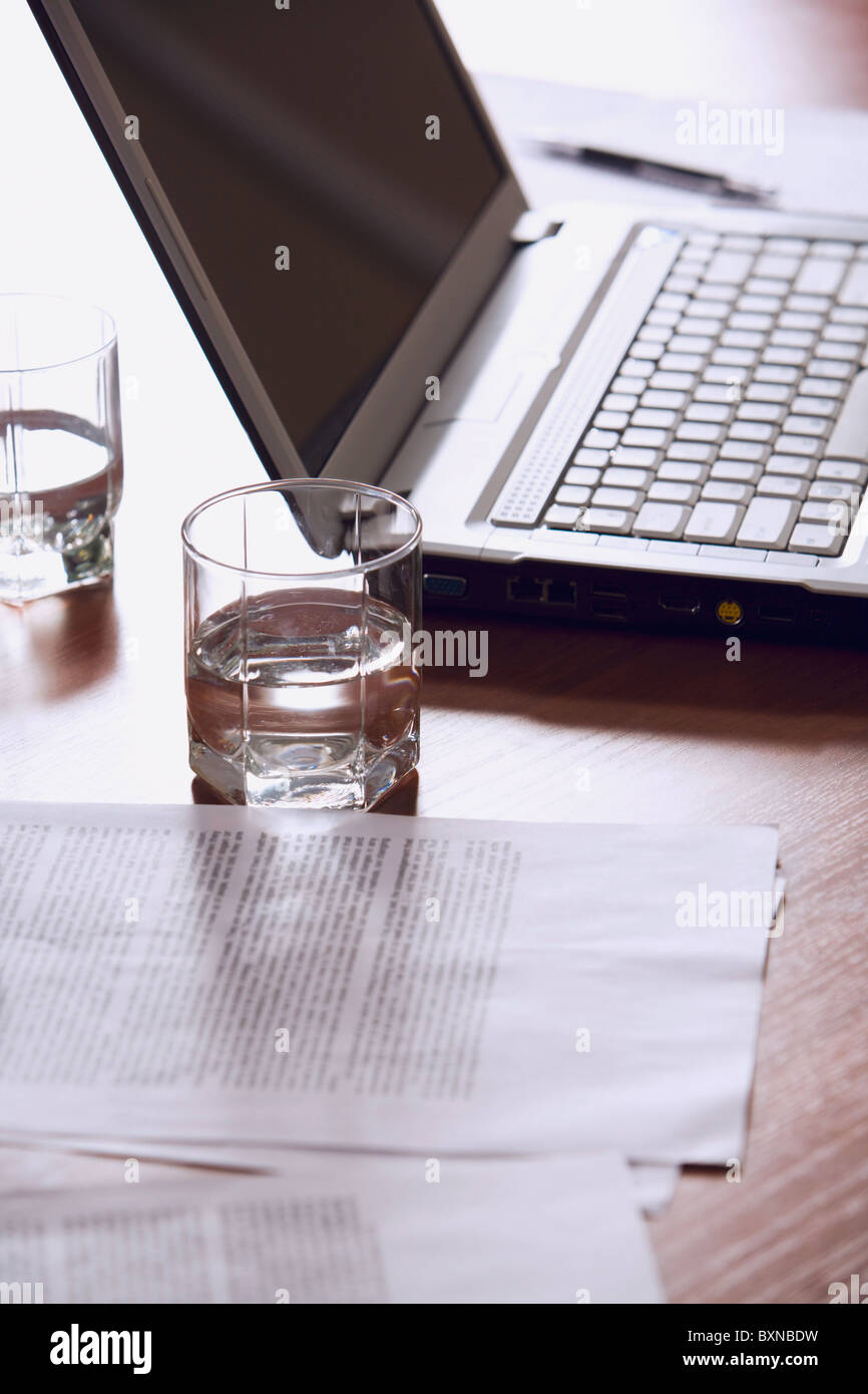 Customary workplace: laptop, papers, pen and glasses of water on a table. Stock Photo