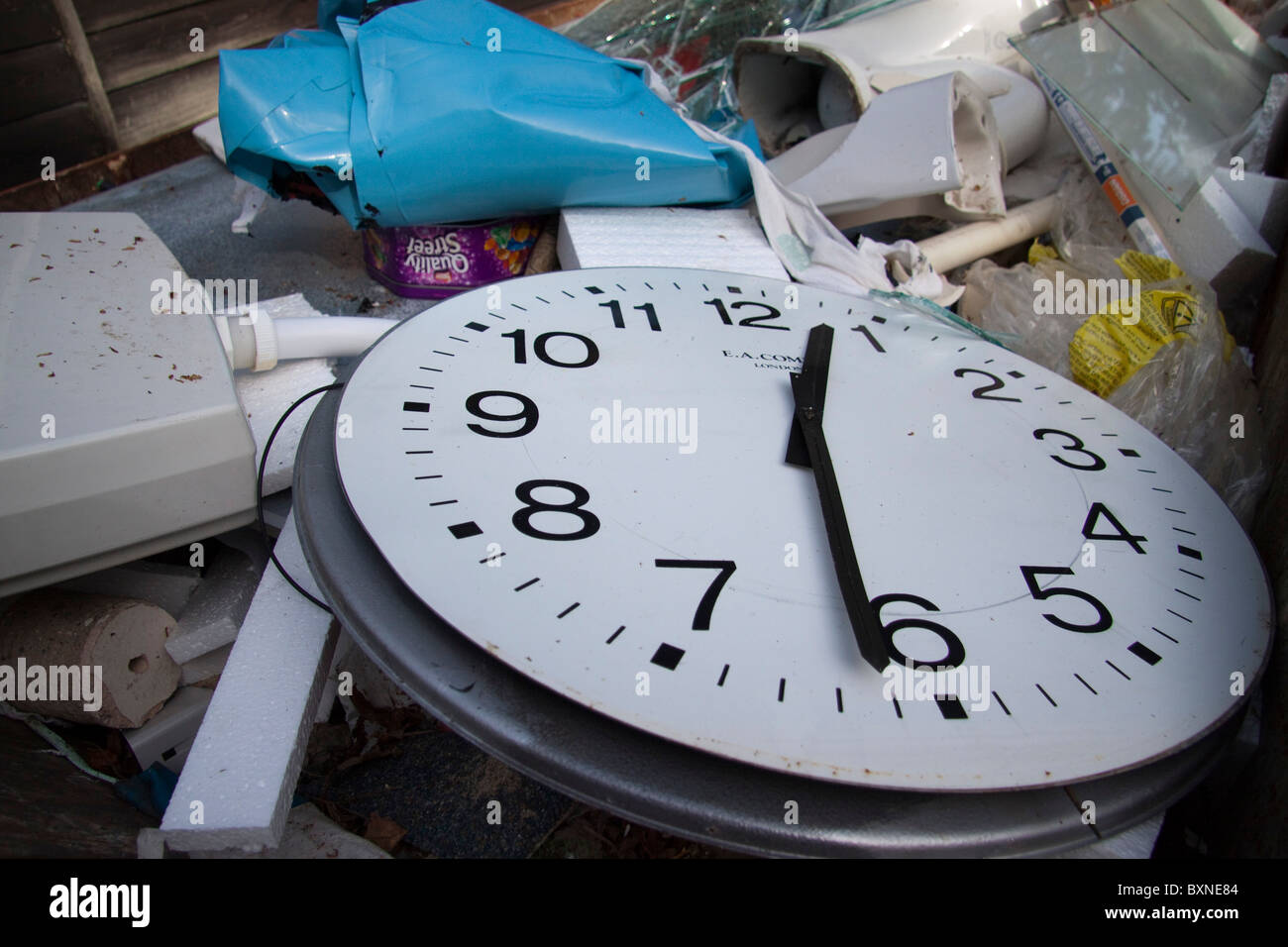 A large clock face with the hands at 12:31 on a pile of rubbish. Stock Photo
