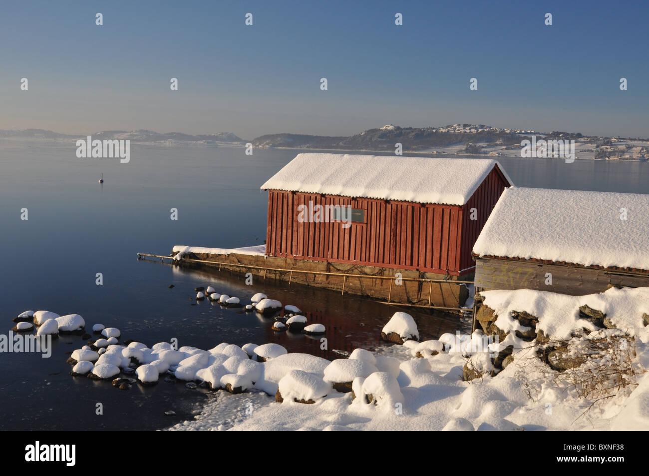 Red boat house by the sea, winter, snow, blue sky, sun, frozen sea Stock Photo