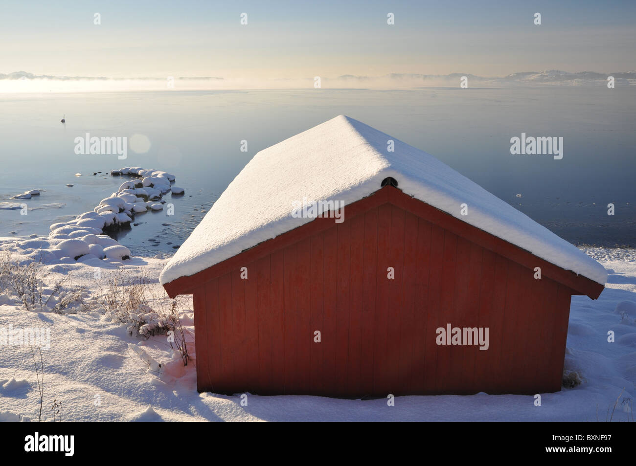 Red boat house by the sea, winter, snow, blue sky, sun, frozen sea Stock Photo