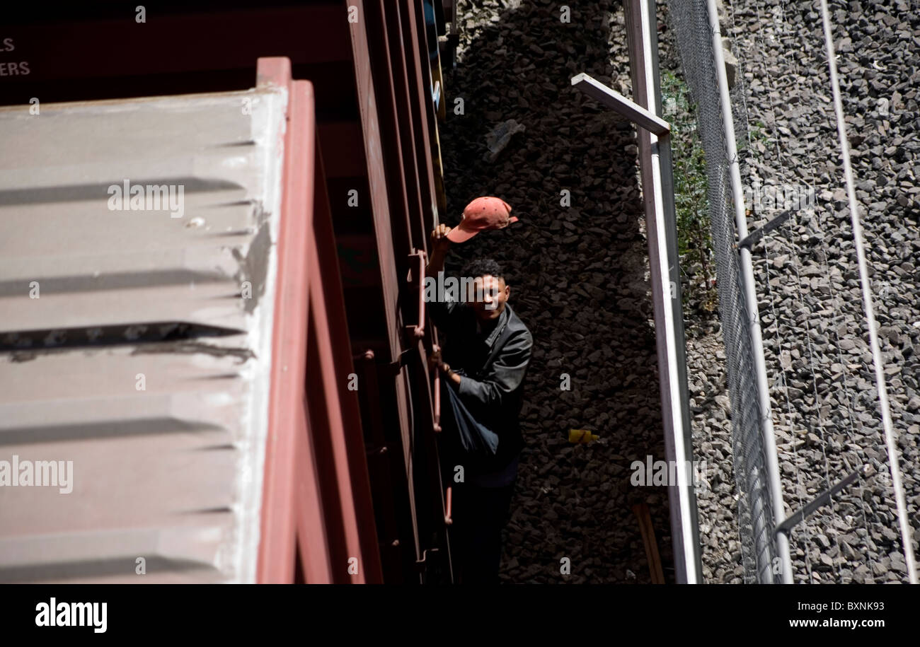 An undocumented Central American migrant salutes with his cap as he holds on a moving train in Mexico City Stock Photo