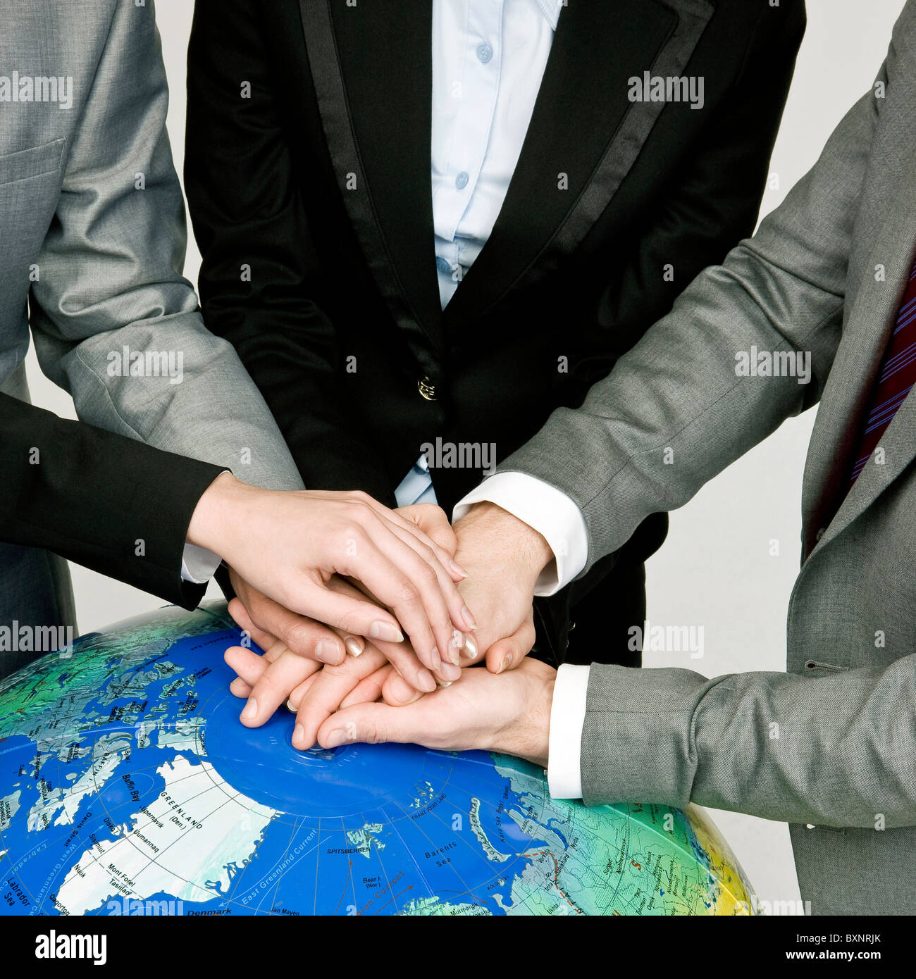 Four business people overlapping hands over globe, elevated view Stock Photo