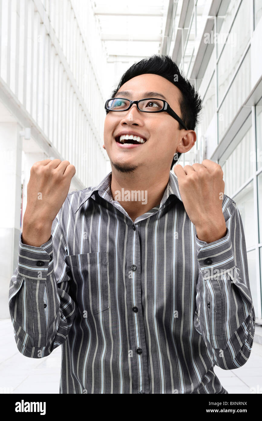 Success winner Asian businessman looking up, office building as background. Stock Photo