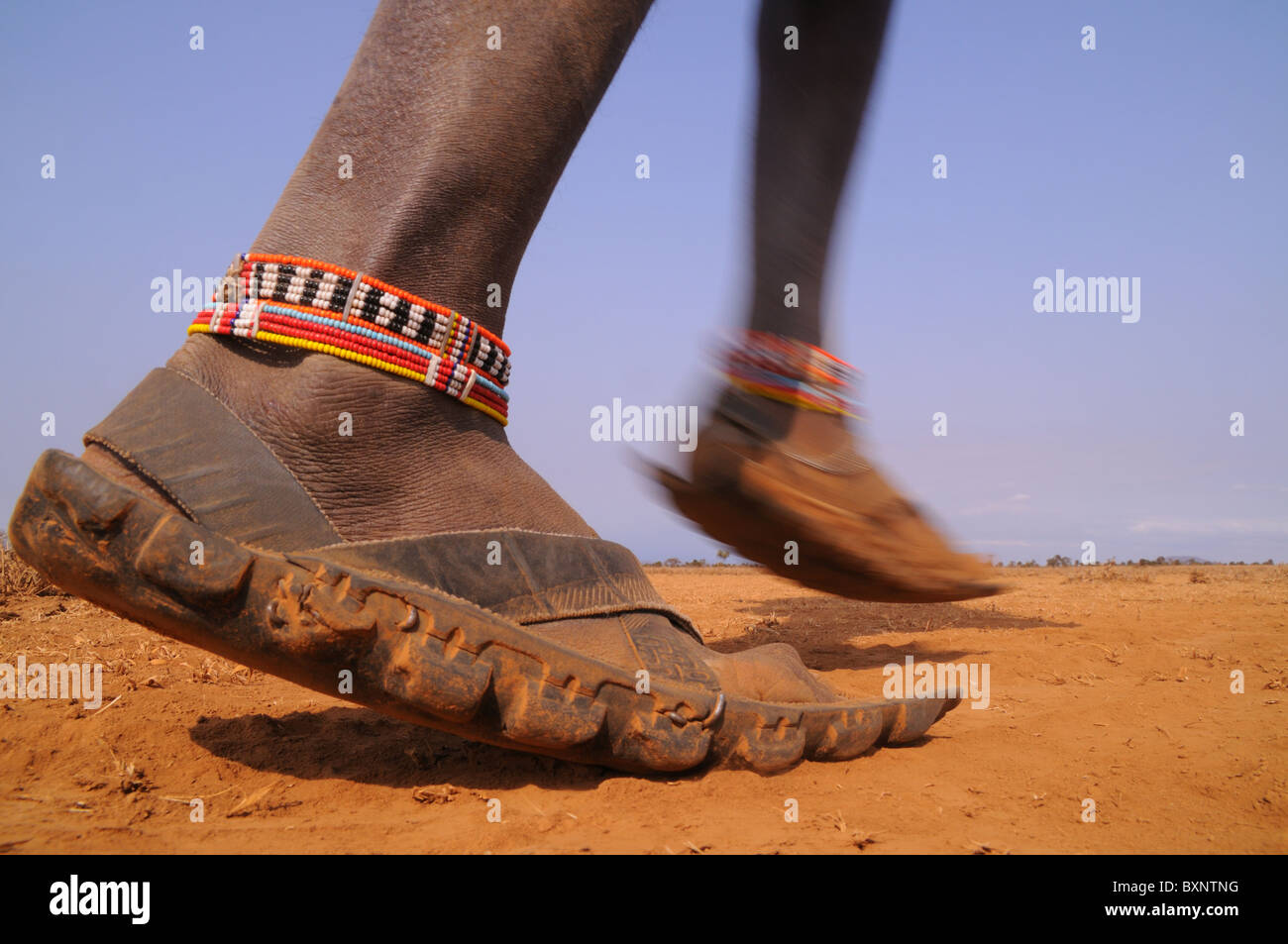 A Maasai warrior walks across the dusty and arid landscape wearing his rubber shoes, uniquely made out of old tyres. Stock Photo