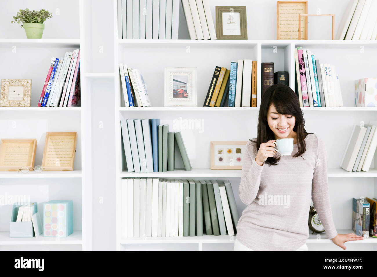 Young woman holding tea cup by bookshelf Stock Photo Alamy