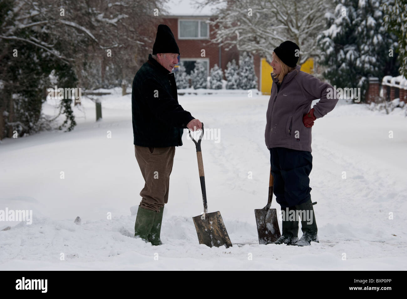 Two neighbours pause in their work clearing snow to chat over their shovels after a heavy snow in Oxford. Stock Photo