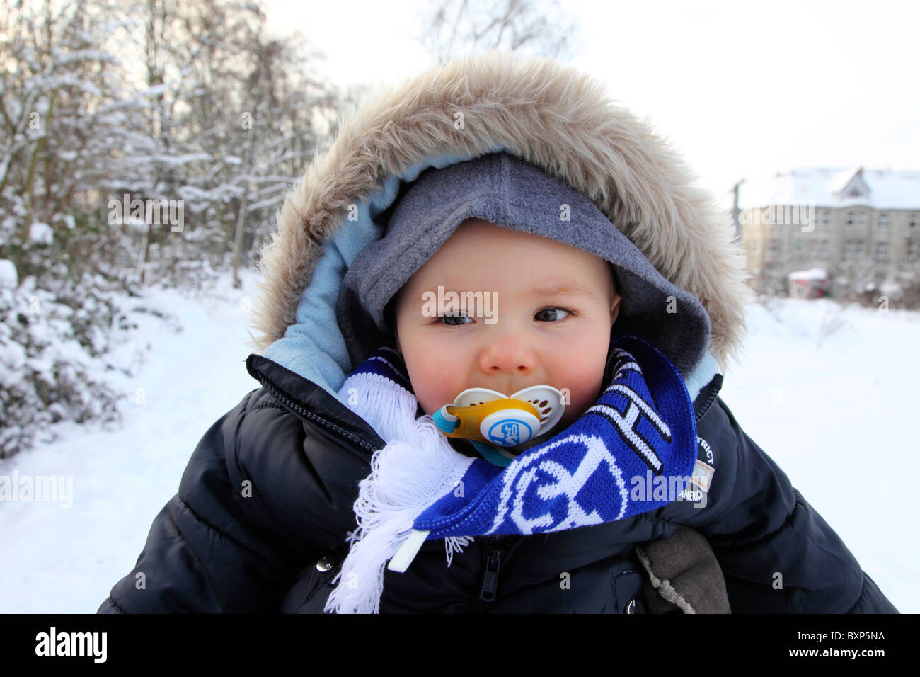 6 month old little boy on the back of his mother, on a walk  in winter, snow, smiling, looking happy and friendly. Stock Photo