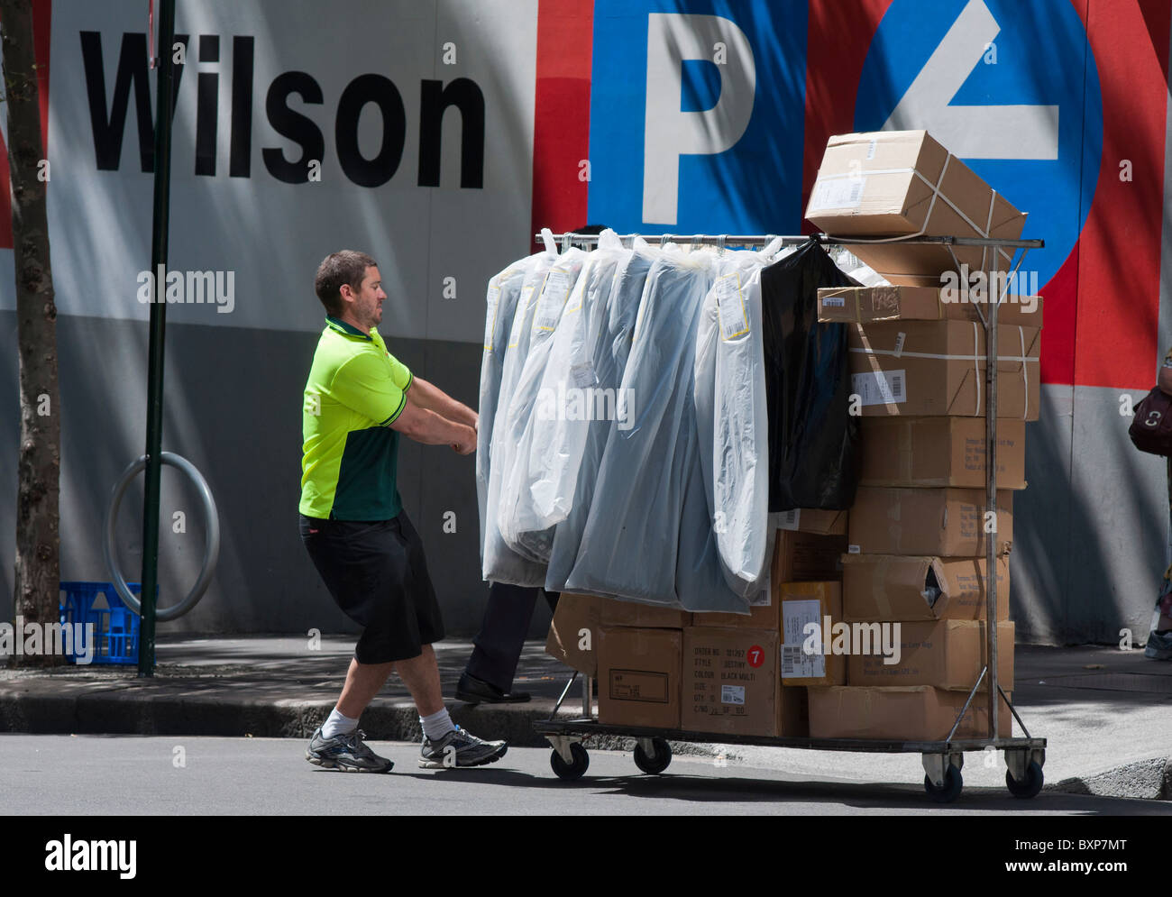 Courier delivering a heavy load of fashion and boxes on a trolley in a city street in Sydney Australia Stock Photo