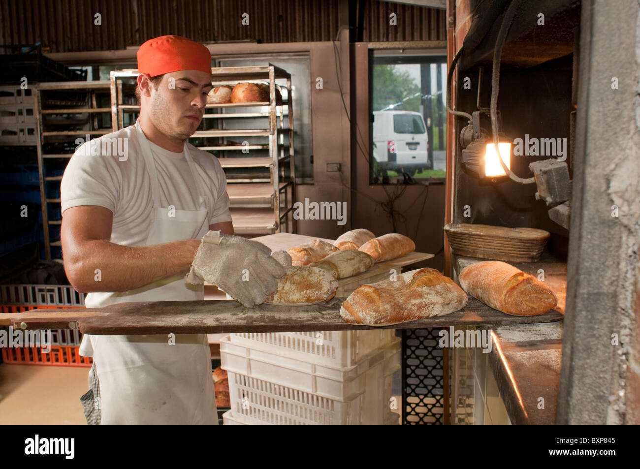 Artisan sourdough baker removing freshly baked bread from a woodfired oven Stock Photo