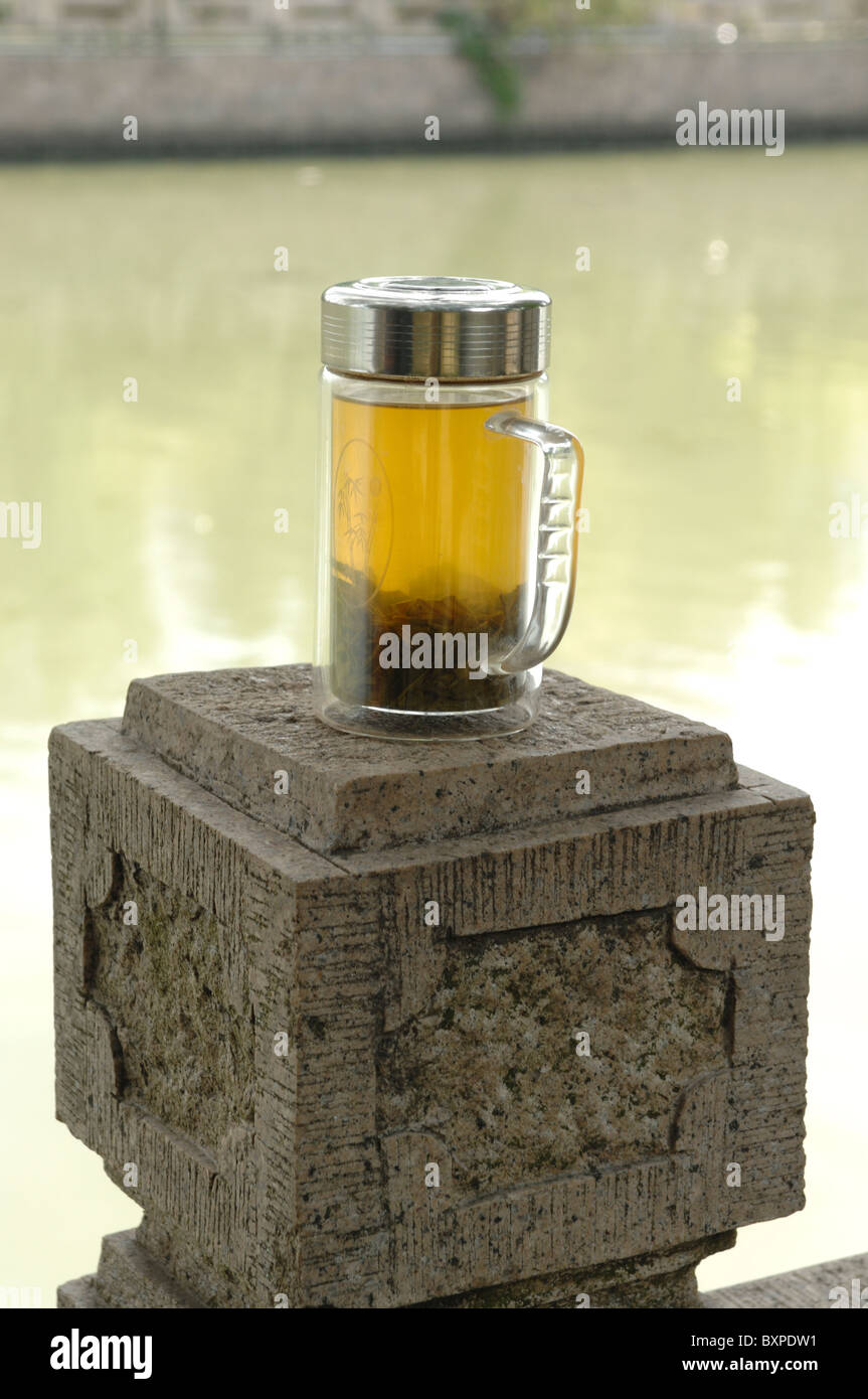 A traditional glass mug of Chinese green tea on a stone plynth by teh Grand Canal in Yangzhou Jiangsu Province of China Stock Photo