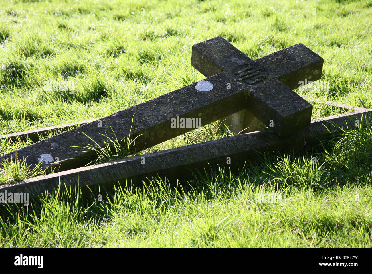 Reclining stone cross headstone on a grave sunlit in a plain grass graveyard Stock Photo