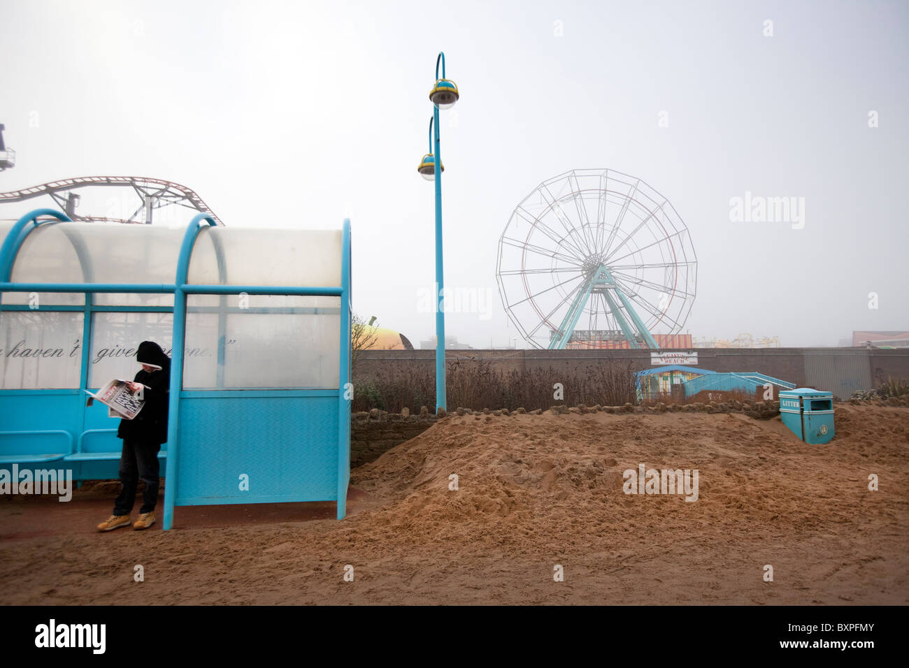 A man reading a newspaper shelters from the winter weather on the sea front at Skegness, UK. Stock Photo