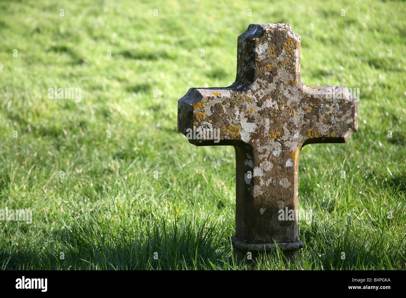 A stone cross headstone sunlit in a plain grass graveyard Stock Photo