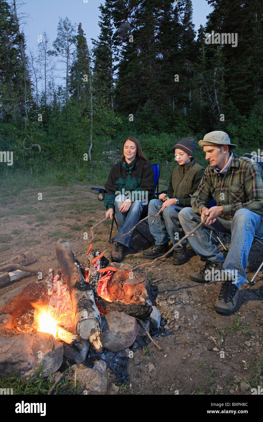 young family of three camping and roasting hot dogs over a fire Stock