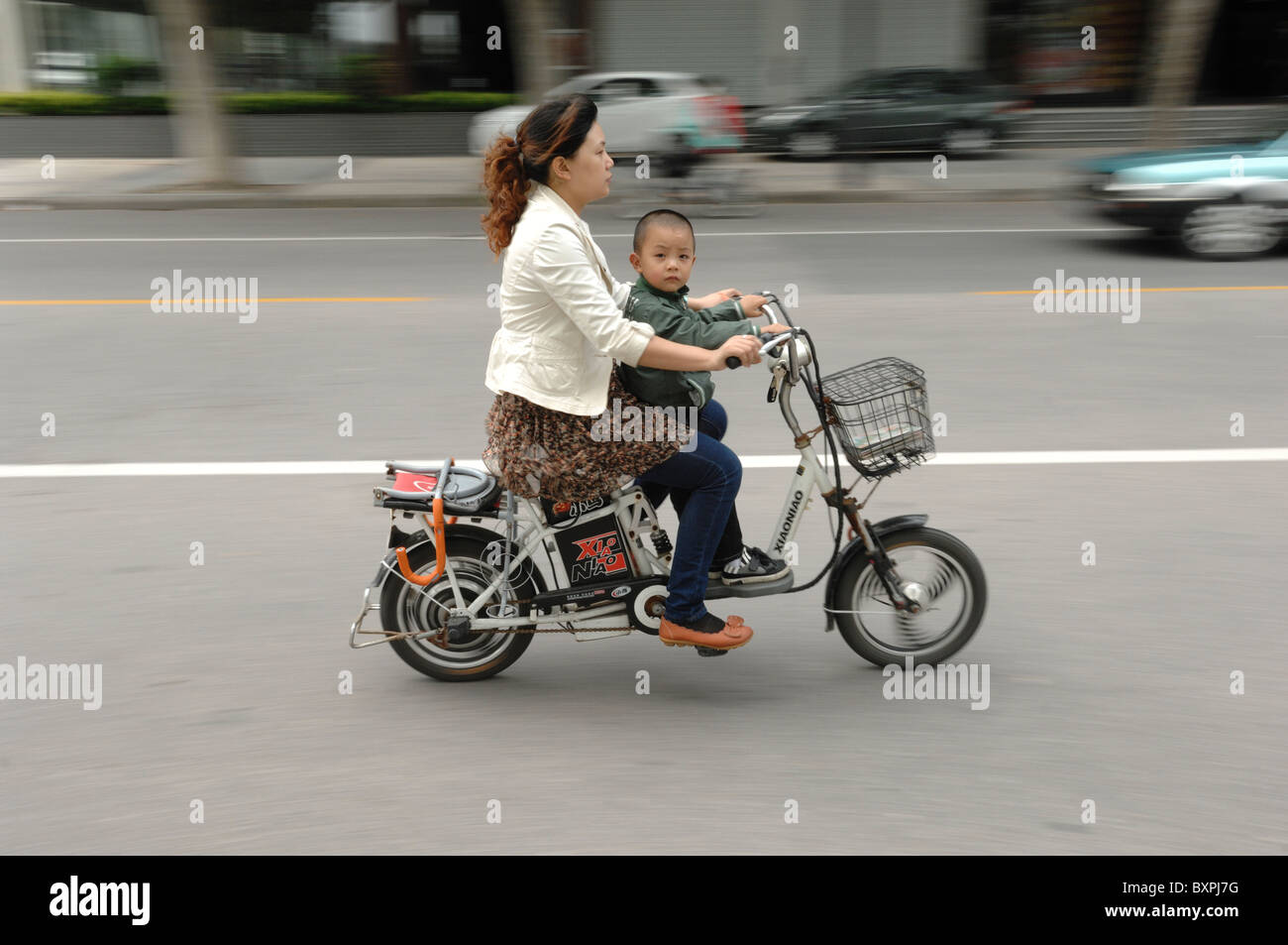 A woman and young child riding an electric scooter along a road in Yangzhou Jiangsu Province of