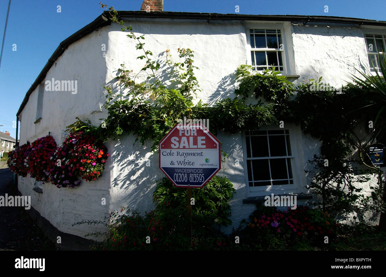 An old whitewashed cottage in a Cornish village with a for sale sign. Stock Photo