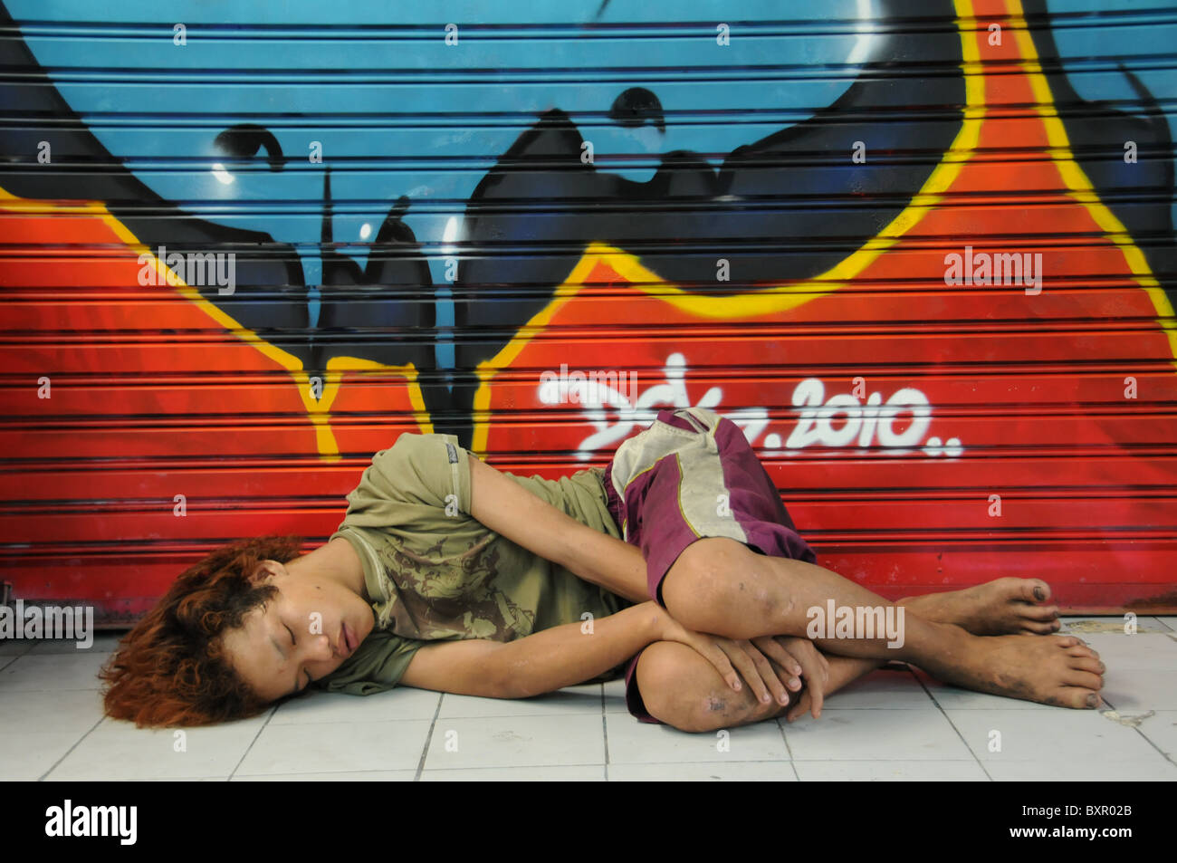 Poor Boy sleeping infront of a Grafitti on the Floor Stock Photo