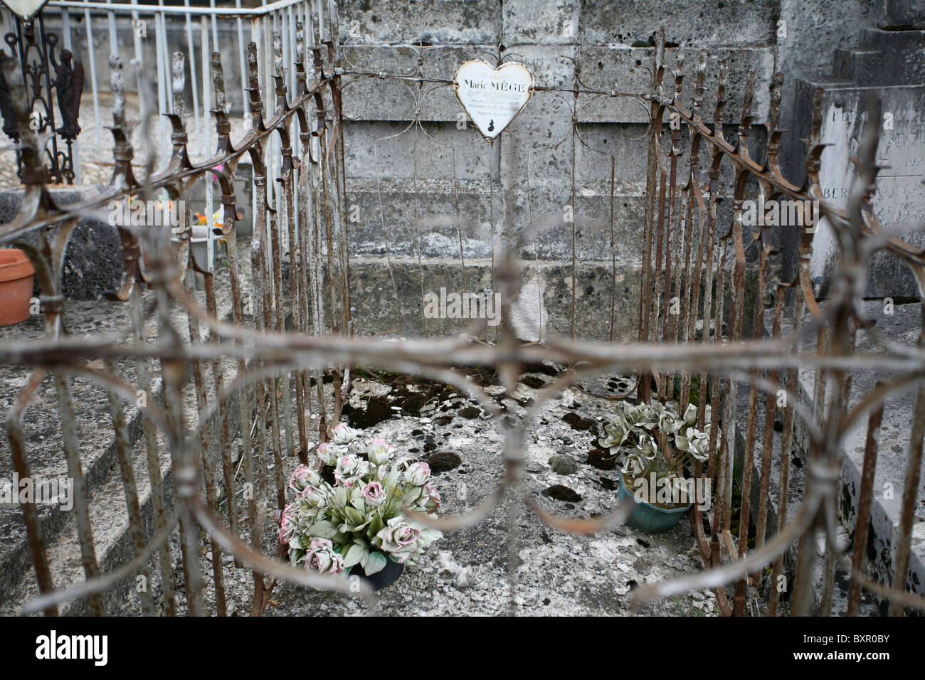 Old cemented tomb enclosed by decorative metal railings with heart nameplate & 2 weathered fake potted plants, Cimetière de Die Stock Photo