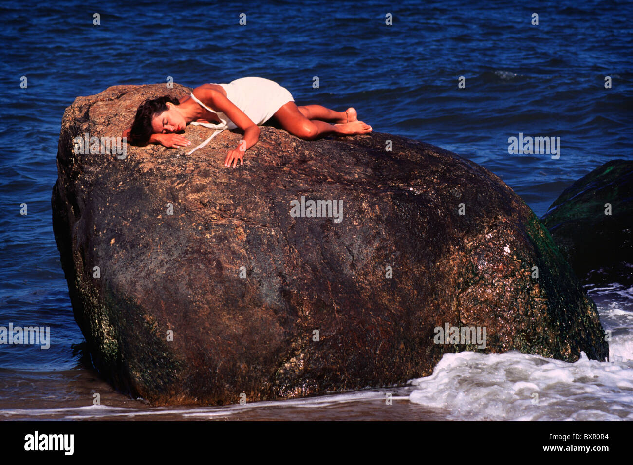 Young woman lying on stone. Ocean in background.20s, 30s, 25-29, 30-34, years old. North Folk. Long Island, New York. Stock Photo