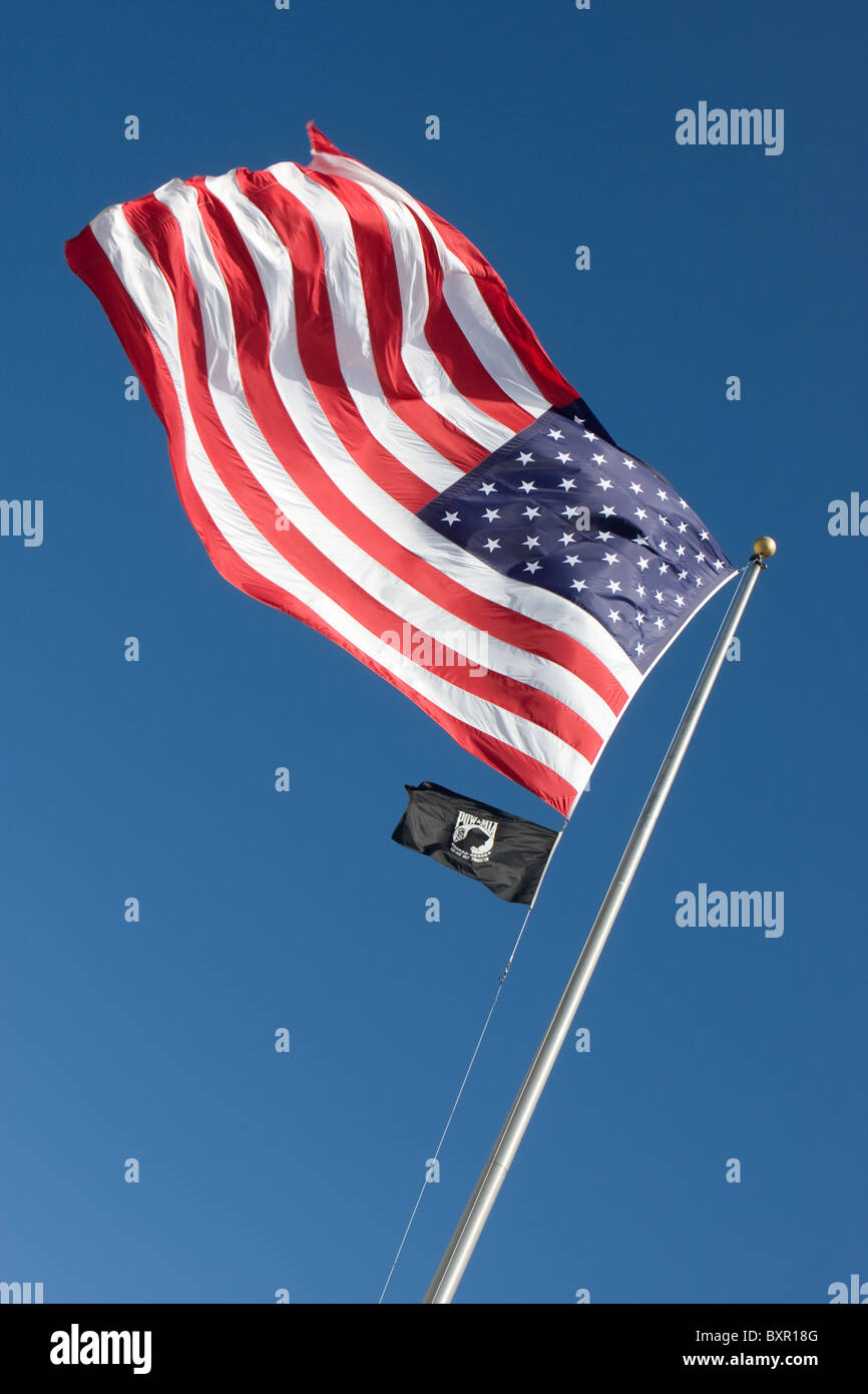 An American flag flaps in the wind against a blue sky along with a smaller POW-MIA flag below. Stock Photo