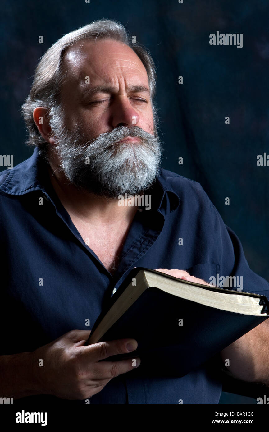 Bearded man praying while holding Holy Bible. Stock Photo