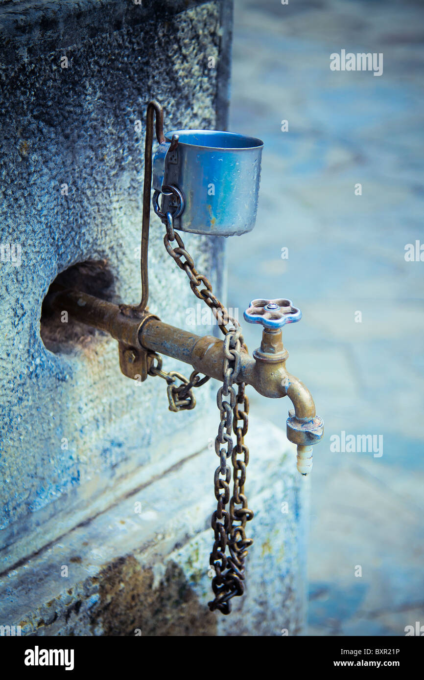 Vertical view of a old water tap with a metal cup. Stock Photo