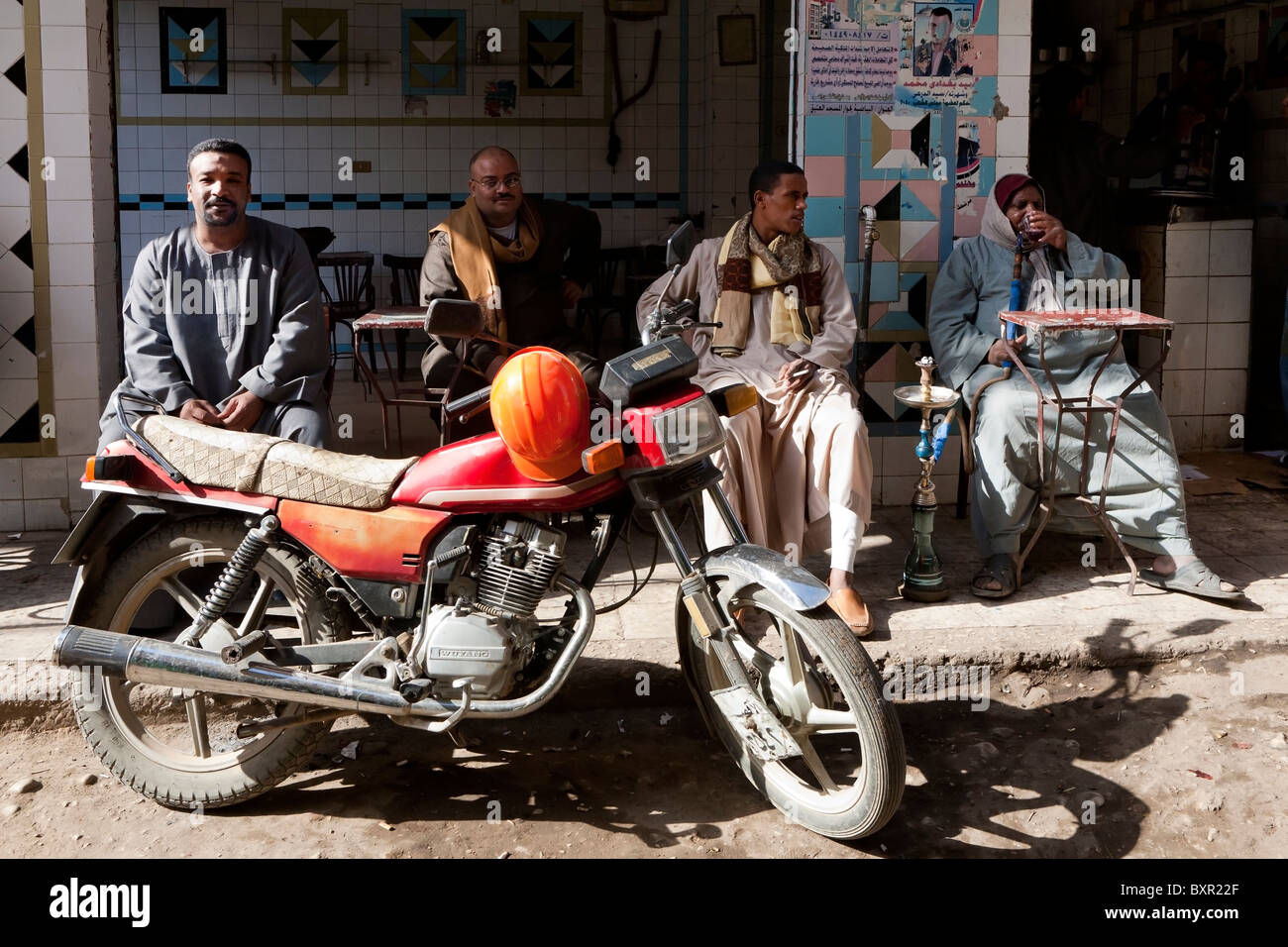 Four men relaxing in cafe behind parked motorbike in local street market, Luxor, Egypt, Africa Stock Photo