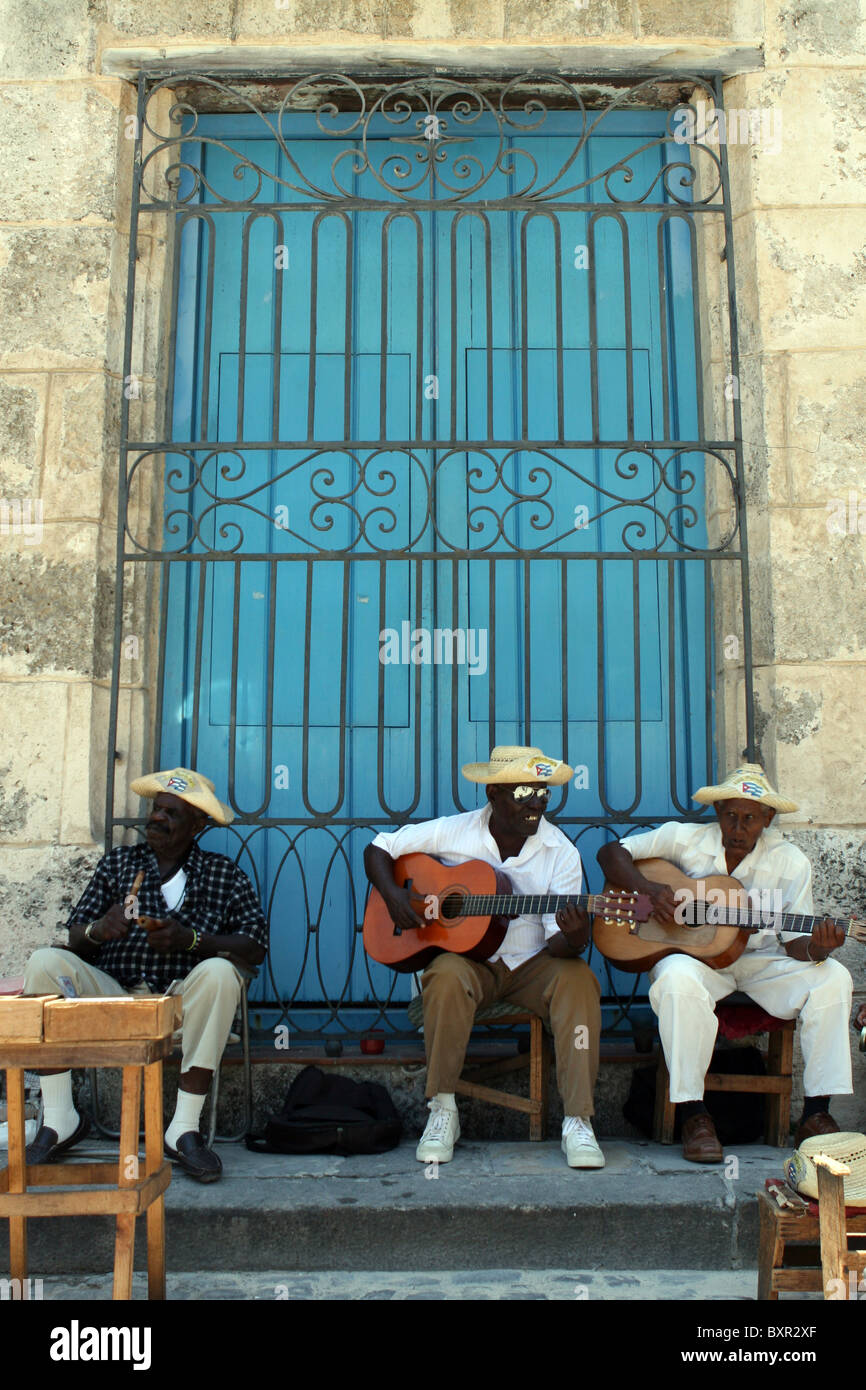 Three men from Los Cambasinos street band, playing outside a big blue door in  Plaza de la Catedral, Havana, Cuba. Stock Photo