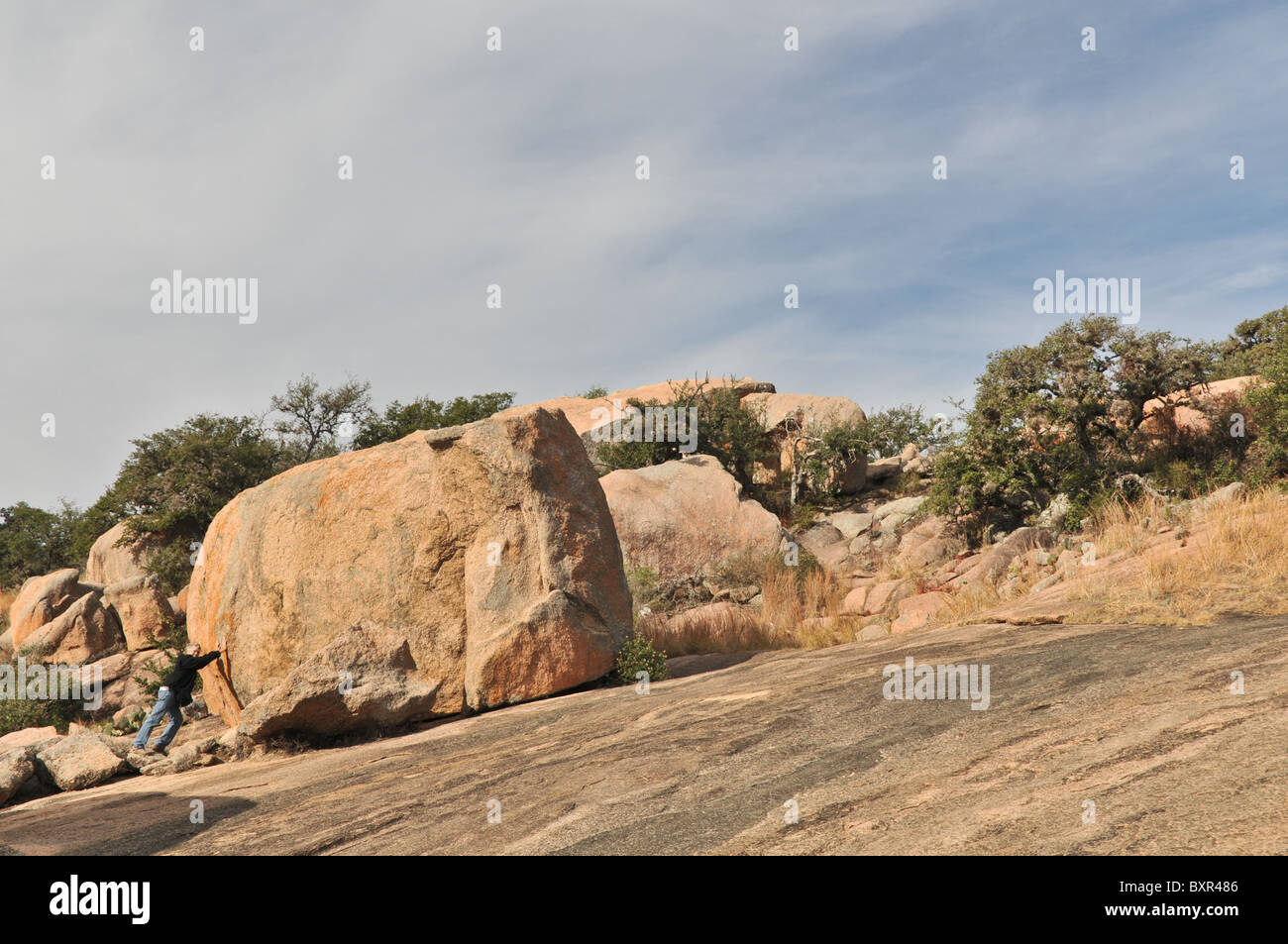 Man attempting to push large exfoliation block on granite batholith, Enchanted Rock Natural Area, Fredricksburg, Texas Stock Photo