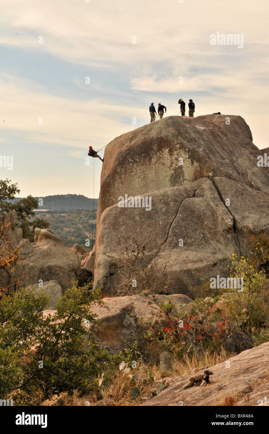Man rappelling down large boulder on granite batholith, Enchanted Rock Natural Area, Fredricksburg, Texas Stock Photo