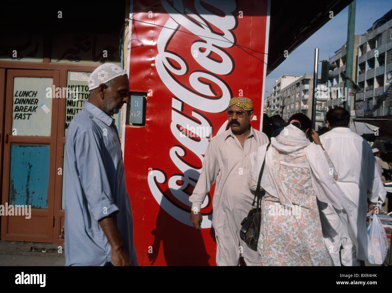 Local Pakistani residents walk past a Coca-Cola advertisement in downtown Karachi, Pakistan. Stock Photo